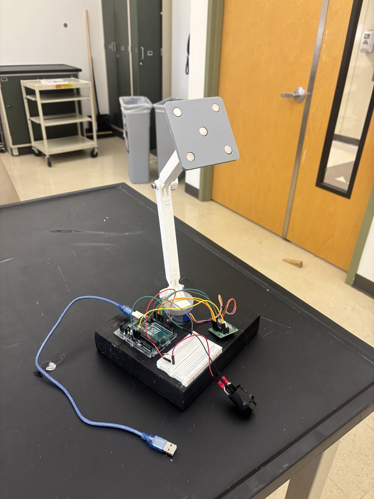 Assembled pick-and-place robot with a white arm, magnetic pickup plate, Arduino, and wired electronics